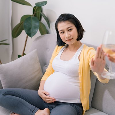 A pregnant woman sitting on a couch refusing an offered glass of wine